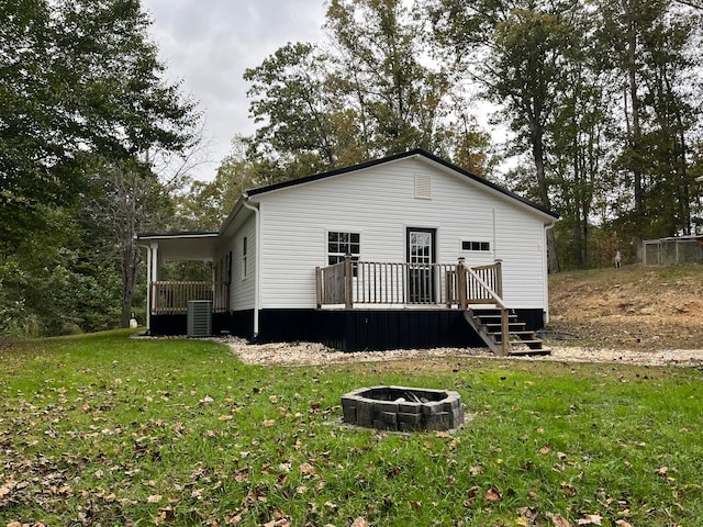 rear view of house with cooling unit, an outdoor fire pit, a deck, and a lawn