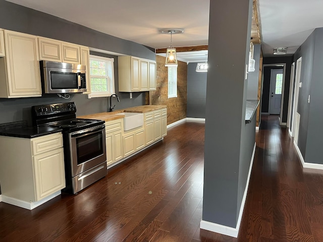 kitchen with sink, cream cabinetry, hanging light fixtures, stainless steel appliances, and dark hardwood / wood-style floors