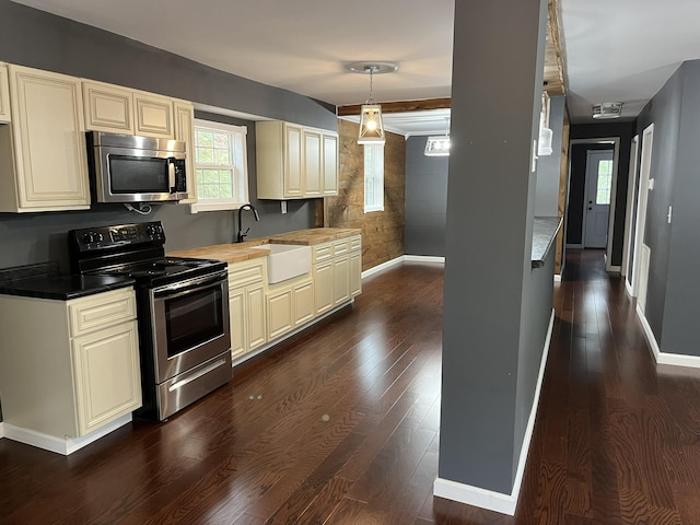 kitchen featuring cream cabinets, appliances with stainless steel finishes, baseboards, and a sink
