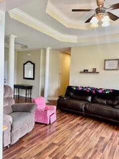 living room featuring ornate columns, wood-type flooring, a raised ceiling, and crown molding