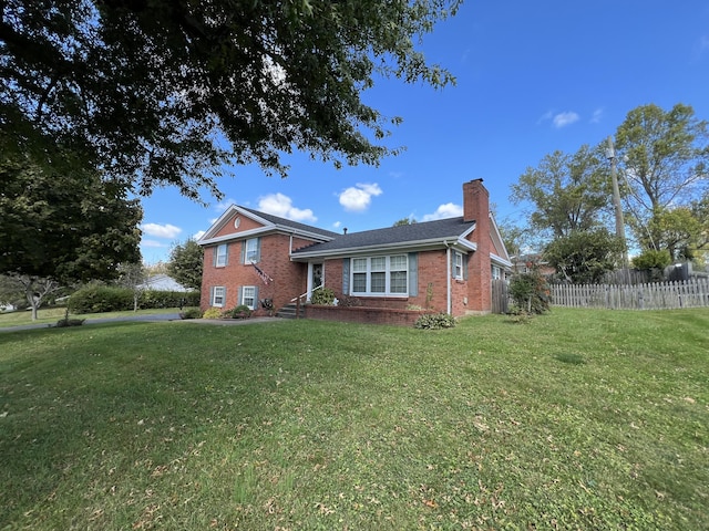 tri-level home with fence, a chimney, brick siding, and a front yard