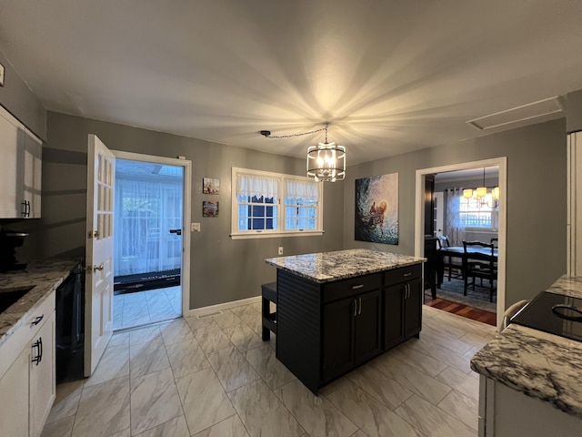 kitchen featuring marble finish floor, light stone counters, dark cabinets, a center island, and a chandelier