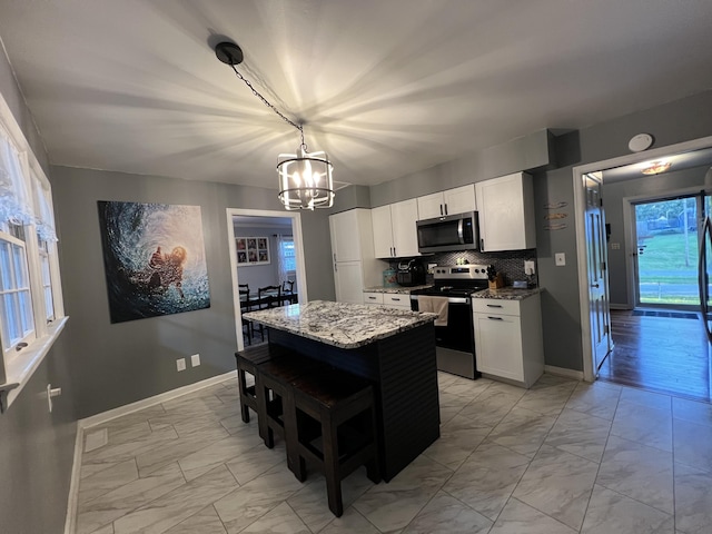 kitchen featuring marble finish floor, appliances with stainless steel finishes, baseboards, and a notable chandelier