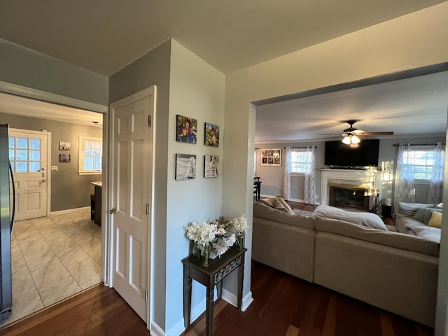living room with ceiling fan, a wealth of natural light, baseboards, a fireplace, and dark wood-style flooring