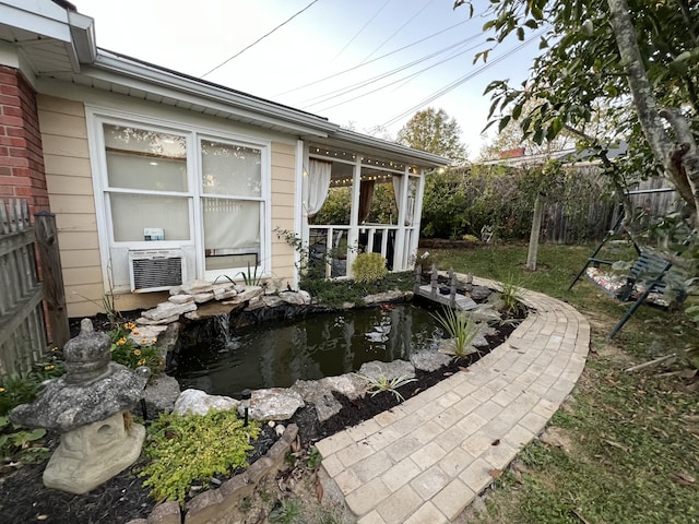 exterior space featuring cooling unit, fence, and a garden pond