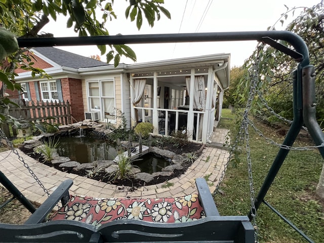 back of house with brick siding, fence, and a garden pond