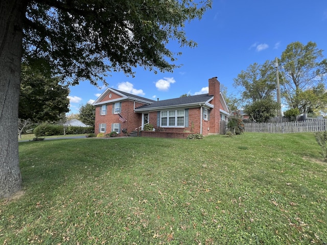 tri-level home with fence, a front lawn, a chimney, and brick siding