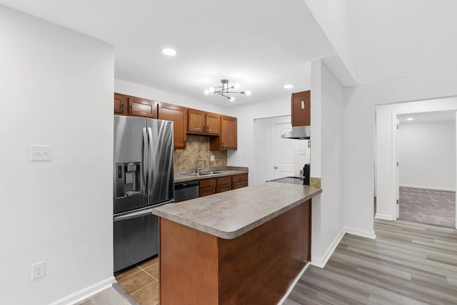 kitchen featuring kitchen peninsula, exhaust hood, appliances with stainless steel finishes, light hardwood / wood-style floors, and sink