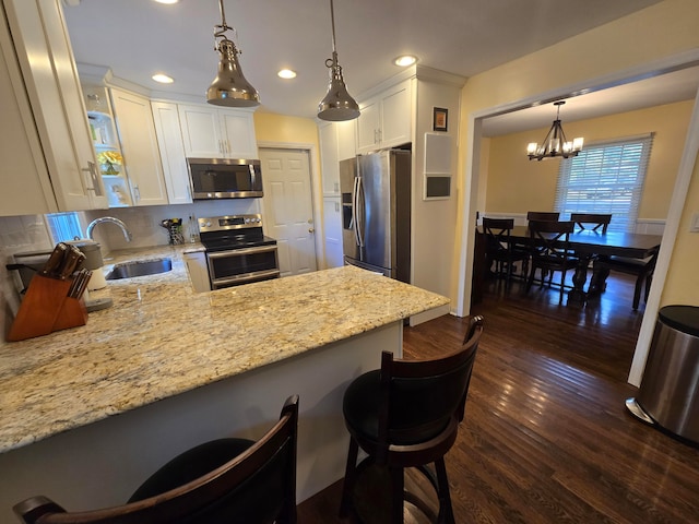 kitchen featuring kitchen peninsula, hanging light fixtures, appliances with stainless steel finishes, a kitchen bar, and dark wood-type flooring