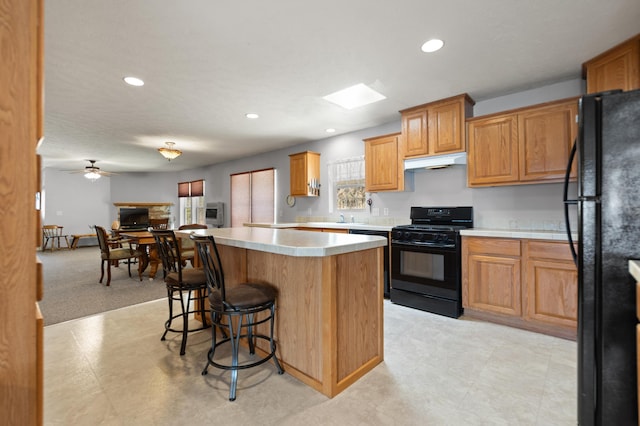 kitchen featuring light carpet, ceiling fan, a kitchen island, a breakfast bar, and black appliances