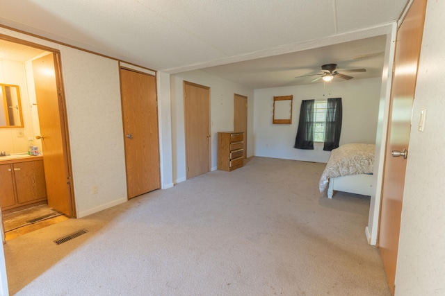 bedroom with light carpet, ensuite bathroom, and ceiling fan