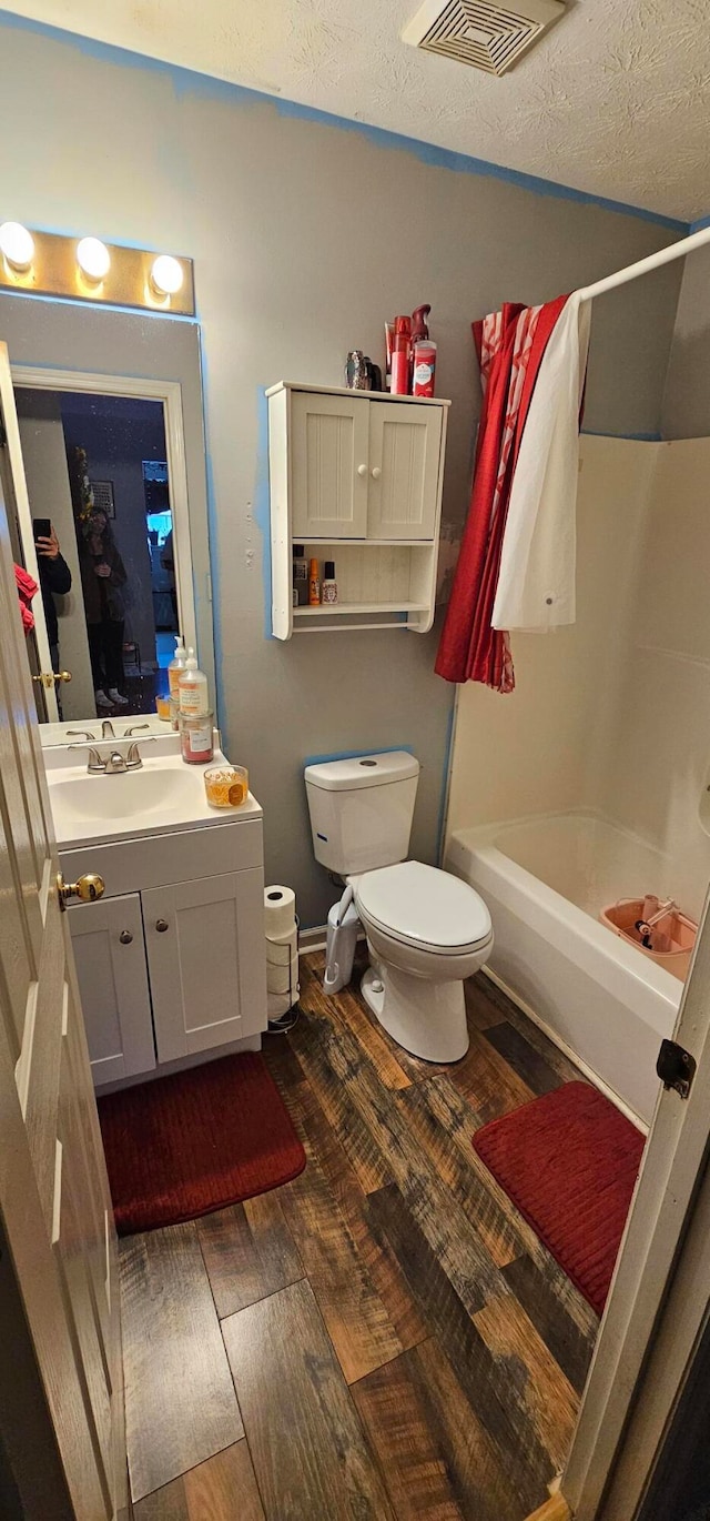 full bathroom featuring toilet, tub / shower combination, hardwood / wood-style floors, vanity, and a textured ceiling