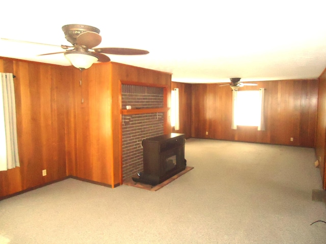 unfurnished living room featuring a wood stove, ceiling fan, and wood walls