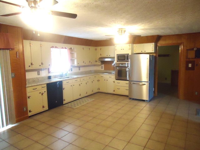 kitchen featuring wood walls, sink, light tile patterned floors, appliances with stainless steel finishes, and white cabinetry