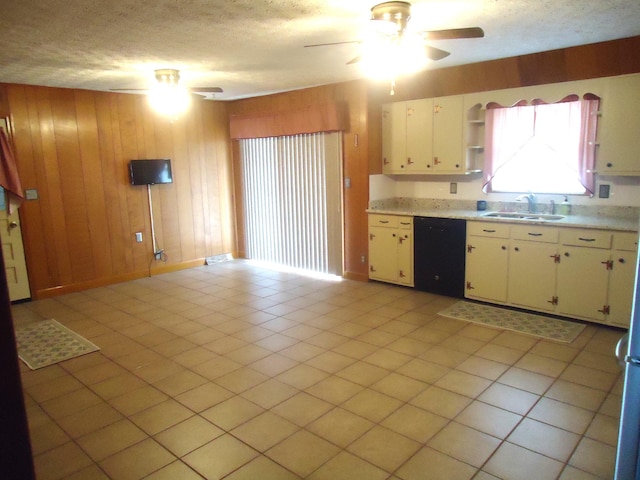 kitchen with white cabinets, sink, wooden walls, light tile patterned floors, and black dishwasher