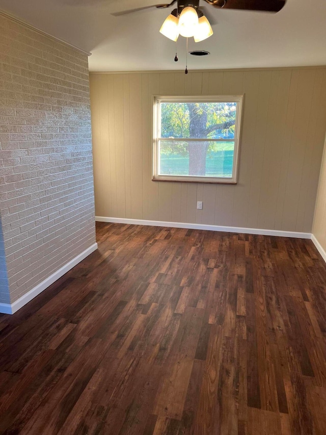 spare room featuring ceiling fan, wooden walls, brick wall, and dark hardwood / wood-style flooring