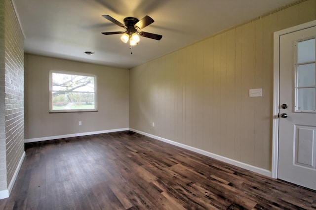 empty room with ceiling fan, wooden walls, and dark hardwood / wood-style floors