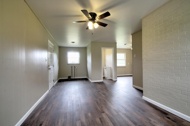 interior space featuring ceiling fan, a wealth of natural light, dark hardwood / wood-style floors, and brick wall