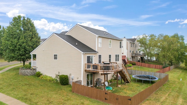 back of property with a wooden deck, a trampoline, and a lawn