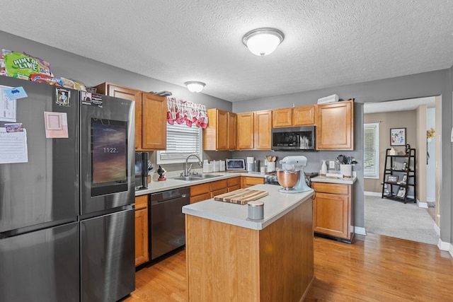 kitchen with appliances with stainless steel finishes, sink, a kitchen island, a textured ceiling, and light hardwood / wood-style floors