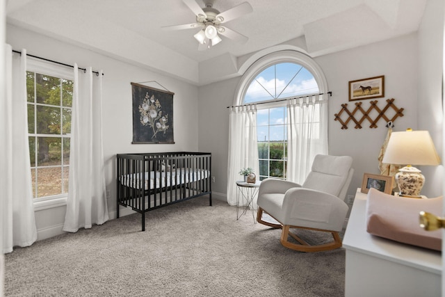 carpeted bedroom with a crib and ceiling fan