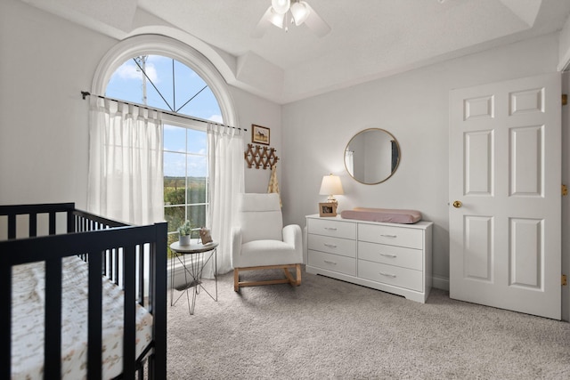 carpeted bedroom featuring a crib and ceiling fan