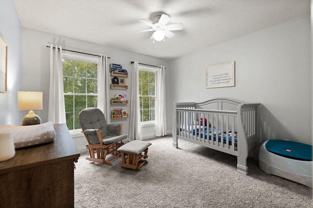 bedroom with a textured ceiling, carpet flooring, a crib, and ceiling fan