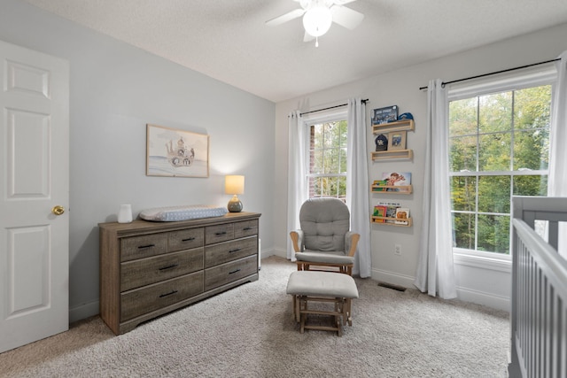 bedroom with ceiling fan, multiple windows, light colored carpet, and a nursery area