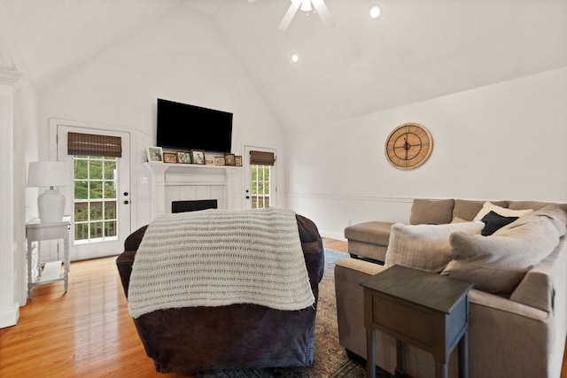 living room with ceiling fan, high vaulted ceiling, light wood-type flooring, and a tile fireplace