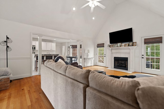 living room featuring high vaulted ceiling, a tile fireplace, light wood-type flooring, and a wealth of natural light