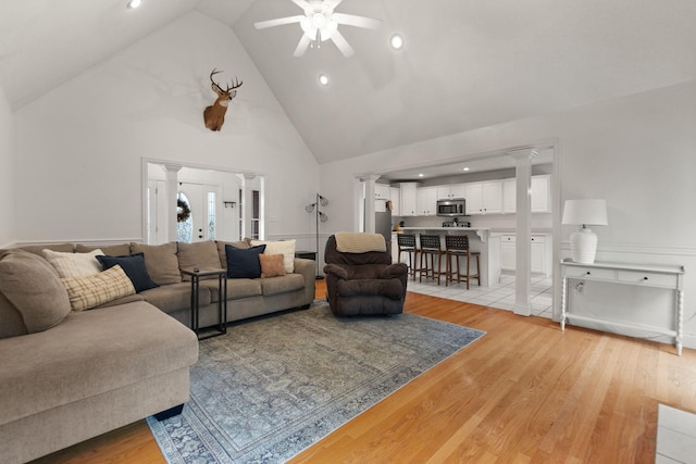 living room with ceiling fan, high vaulted ceiling, decorative columns, and light hardwood / wood-style flooring