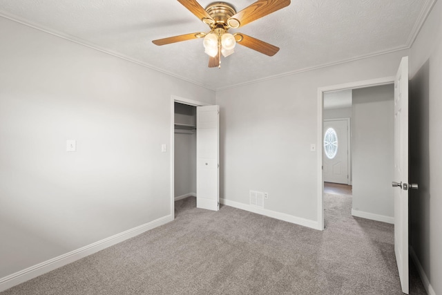 unfurnished bedroom with light carpet, ceiling fan, a textured ceiling, crown molding, and a closet