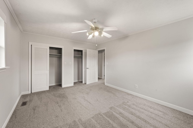 unfurnished bedroom with multiple closets, carpet, crown molding, and ceiling fan