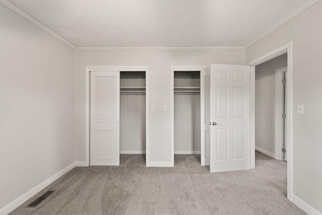 unfurnished bedroom with light carpet, crown molding, multiple closets, and a textured ceiling