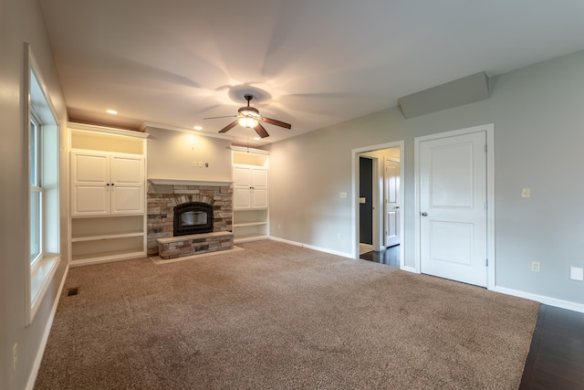 unfurnished living room with a stone fireplace, dark carpet, and ceiling fan