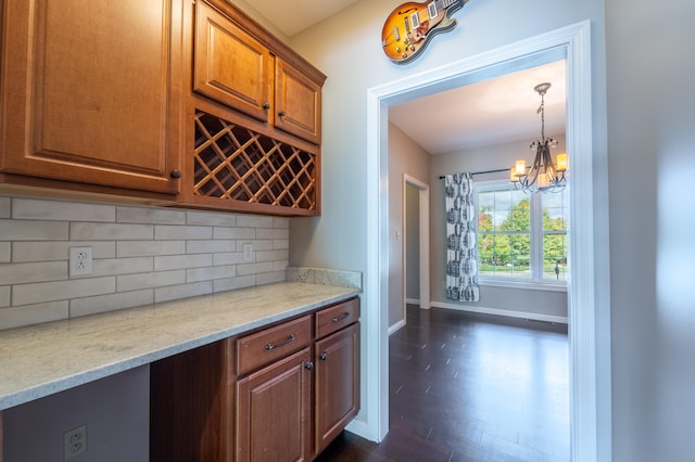 bar featuring decorative backsplash, dark hardwood / wood-style floors, hanging light fixtures, light stone countertops, and a chandelier