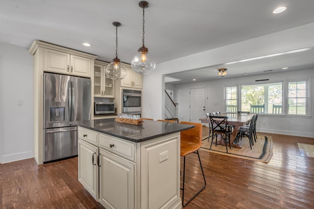 kitchen featuring a kitchen island, cream cabinetry, a breakfast bar, appliances with stainless steel finishes, and dark hardwood / wood-style flooring