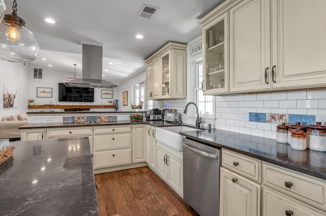 kitchen with cream cabinets, island exhaust hood, pendant lighting, stainless steel dishwasher, and dark stone countertops