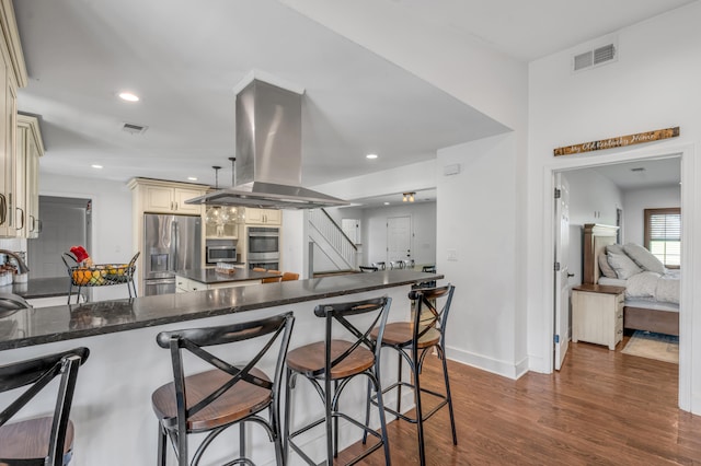 kitchen featuring island exhaust hood, appliances with stainless steel finishes, kitchen peninsula, and cream cabinetry