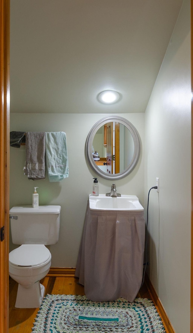 bathroom with toilet, wood finished floors, baseboards, and a sink