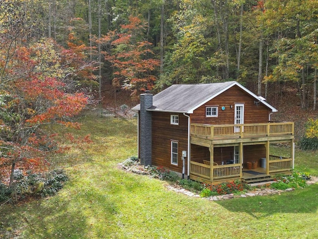 exterior space featuring a deck, a lawn, a wooded view, and a chimney