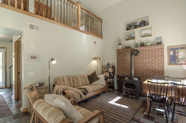 living area with stone tile floors, visible vents, a high ceiling, and a wood stove