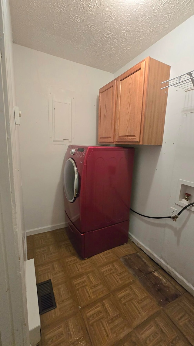 clothes washing area with cabinets, washer / dryer, a textured ceiling, and dark parquet floors