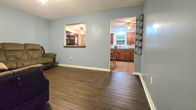 living room with a textured ceiling, ceiling fan, and dark wood-type flooring