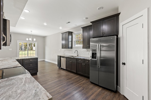 kitchen with light stone countertops, sink, stainless steel appliances, decorative light fixtures, and dark wood-type flooring