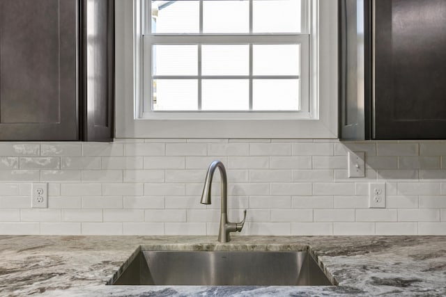 details featuring sink, light stone countertops, dark brown cabinets, and tasteful backsplash