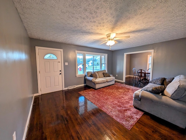 living room with dark wood-type flooring, a textured ceiling, and ceiling fan