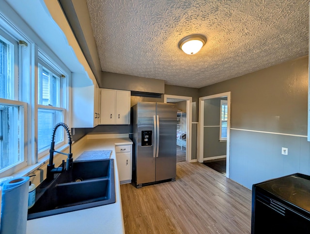 kitchen featuring sink, light wood-type flooring, a textured ceiling, stainless steel fridge, and white cabinetry