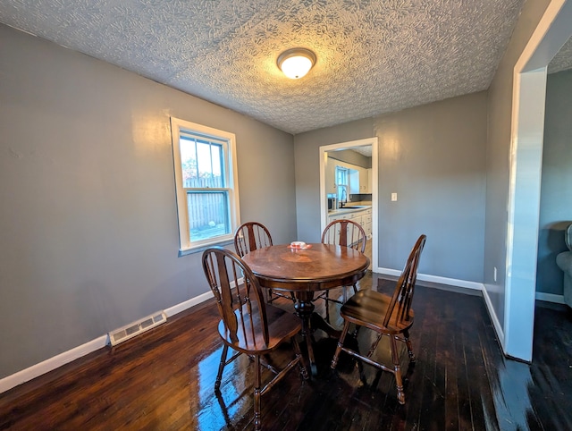 dining space with a textured ceiling, sink, and dark wood-type flooring