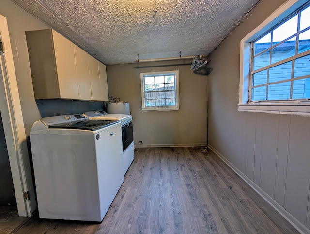 clothes washing area featuring independent washer and dryer, a textured ceiling, water heater, light hardwood / wood-style floors, and cabinets